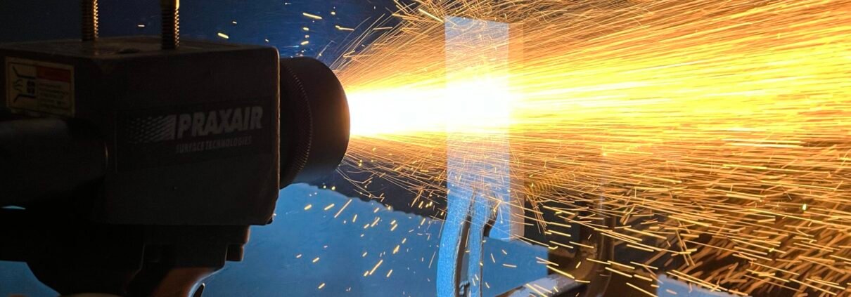 Wire Arc Spray Coating Process A technician using a Praxair Wire Arc Spray system to apply a high-temperature metal coating, producing a bright spray of molten metal particles.