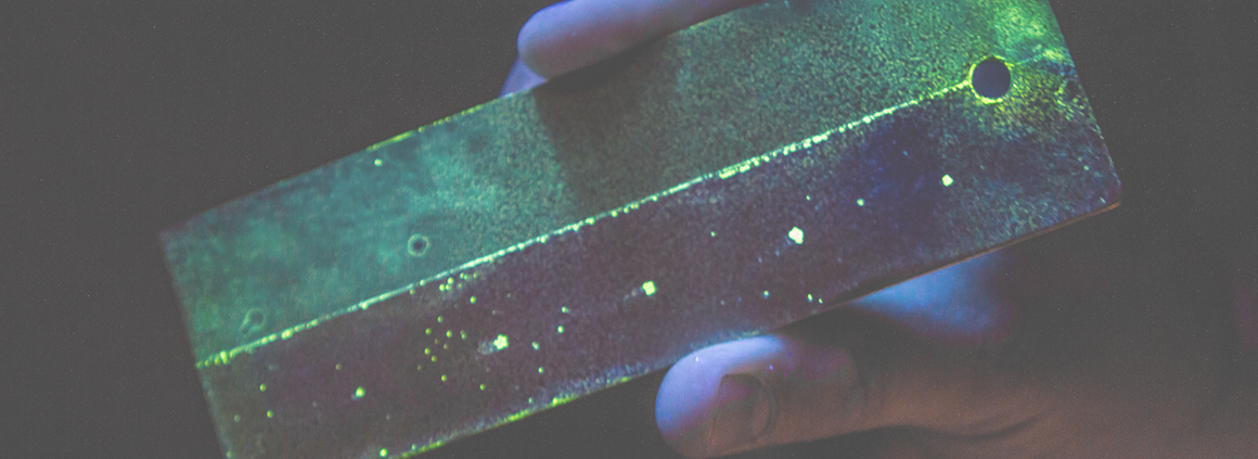Fluorescent Penetrant Inspection (FPI) - Non-Destructive Testing A component undergoing Fluorescent Penetrant Inspection (FPI) under UV light, revealing surface cracks and defects through glowing indications.